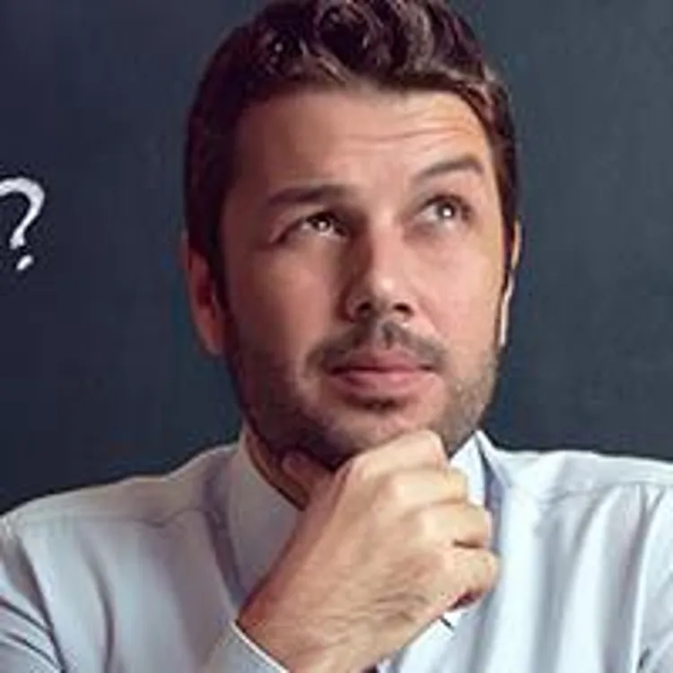 casual businessman thinking in front of a chalkboard filled question marks