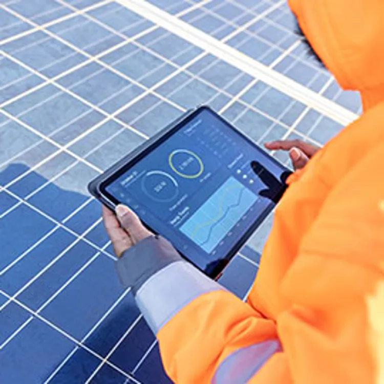 over the shoulder view of a field technician holding a digital tablet showing a solar power panel monitoring app