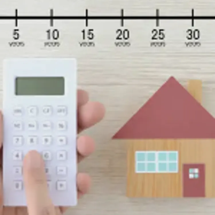 Hand holding small white calculator next to a digital drawing of a brown house with a red roof, red door, and brown chimney.