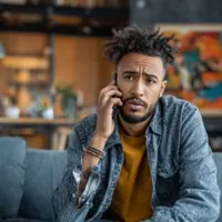 a man answering his cellular phone while sitting on a sofa