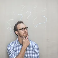 man standing in front of a concrete wall with chalk drawings of question marks