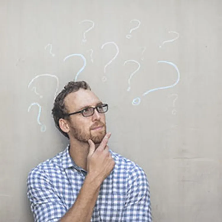 man standing in front of a concrete wall with chalk drawings of question marks