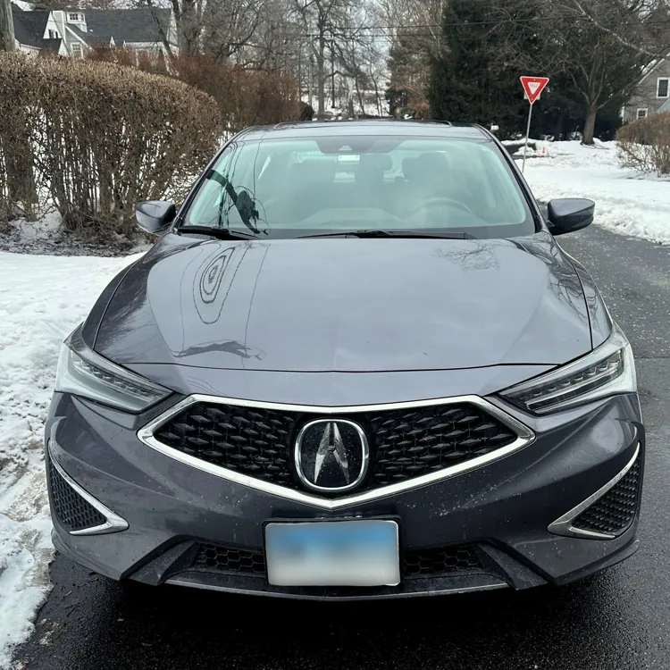 Gray car parked on a snowy suburban street with houses and bare trees in the background.