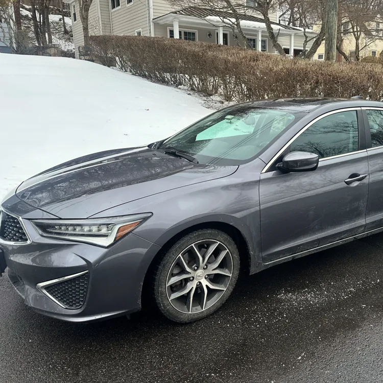 Gray sedan parked on a snowy suburban street with houses and bare trees in the background.
