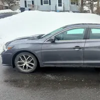 Gray sedan parked on a snowy suburban driveway with houses in the background.