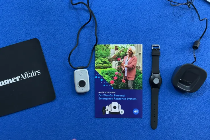 Overhead view of the ADT On-the-Go system: pendant on lanyard, quick setup guide, wristband and charging base