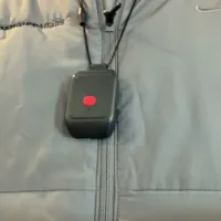 Alert1 LifeBeacon pendant hanging on its black cord lanyard against a gray ConsumerAffairs vest