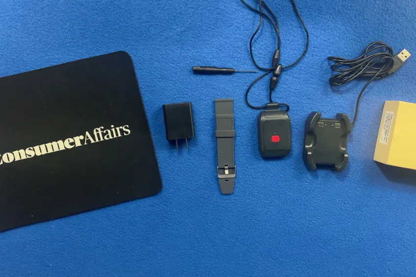 Overhead view of the Alert1 LifeBeacon pendant on its lanyard, charging cradle, USB cable, wall adapter, wristband, screwdriver and box beside a ConsumerAffairs mousepad