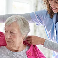 nurse helping put sweater on elderly woman