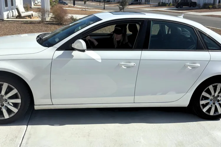 White sedan parked on a suburban driveway with a person sitting inside.