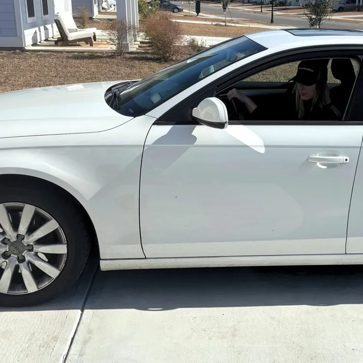 White sedan parked on a suburban driveway with a person sitting inside.