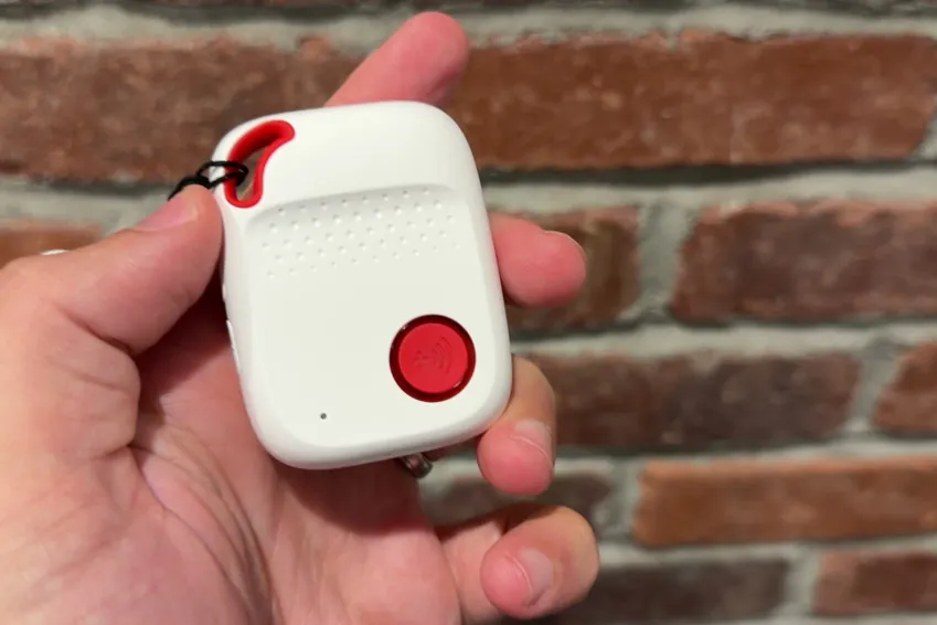 SOS All-in-One 2 pendant with its red help button held in a hand in front of a brick wall