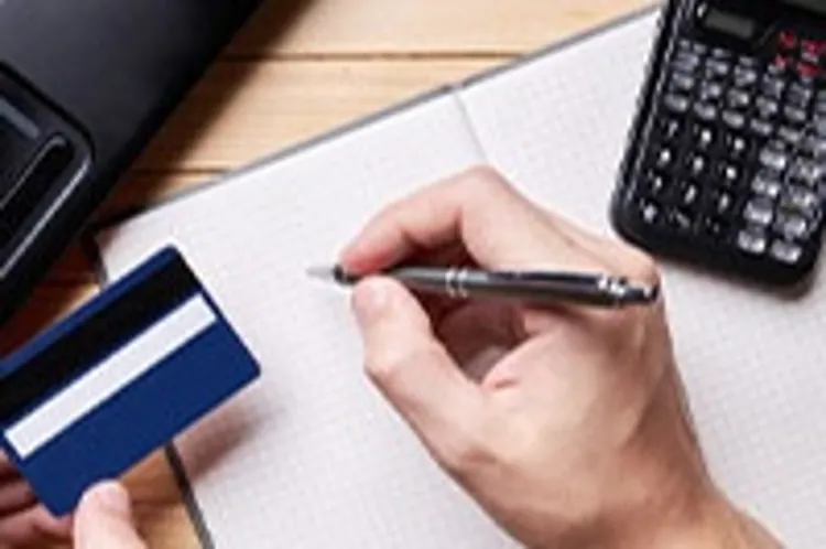 person holding credit card and pen making calculations