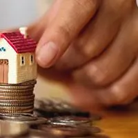 hand putting miniature houses on pile of coins