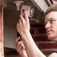 man attaching an outdoor security camera to his house