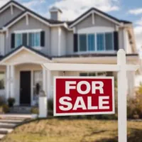 white two-story house with a red 'for sale' sign on the front yard