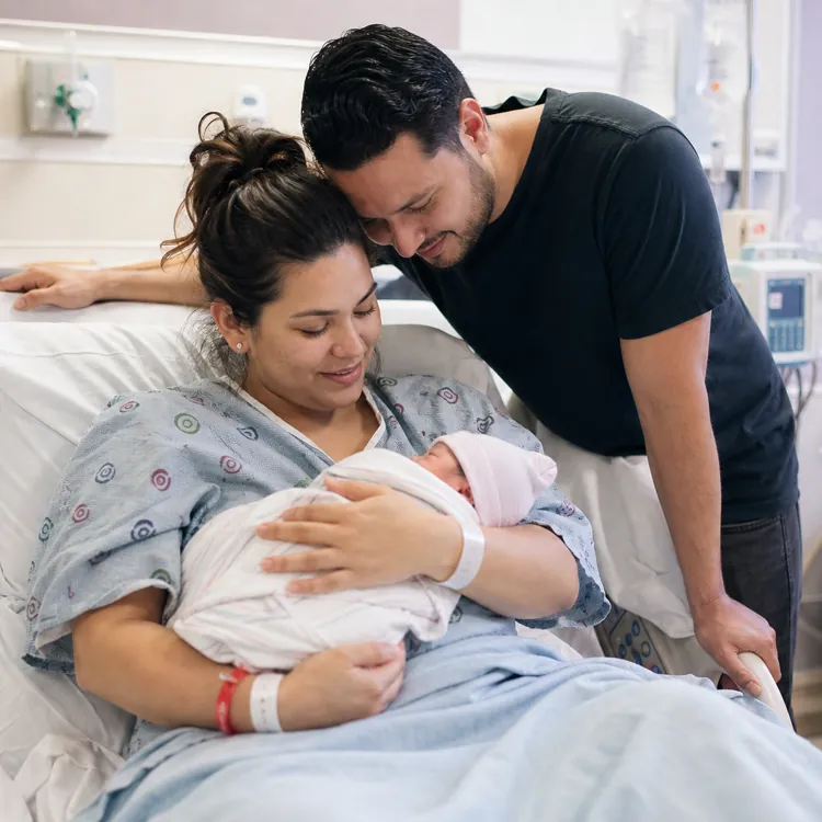 Mother and father smiling at newborn baby in hospital bed