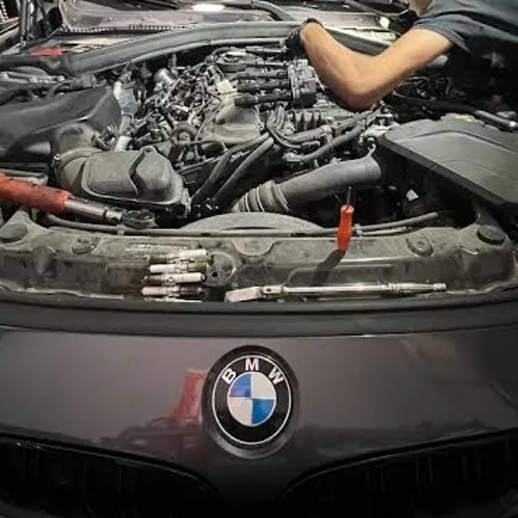 Mechanic working on the engine of a BMW car with the hood open in a workshop