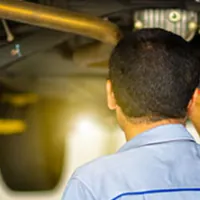 auto mechanic inspecting under chassis of car