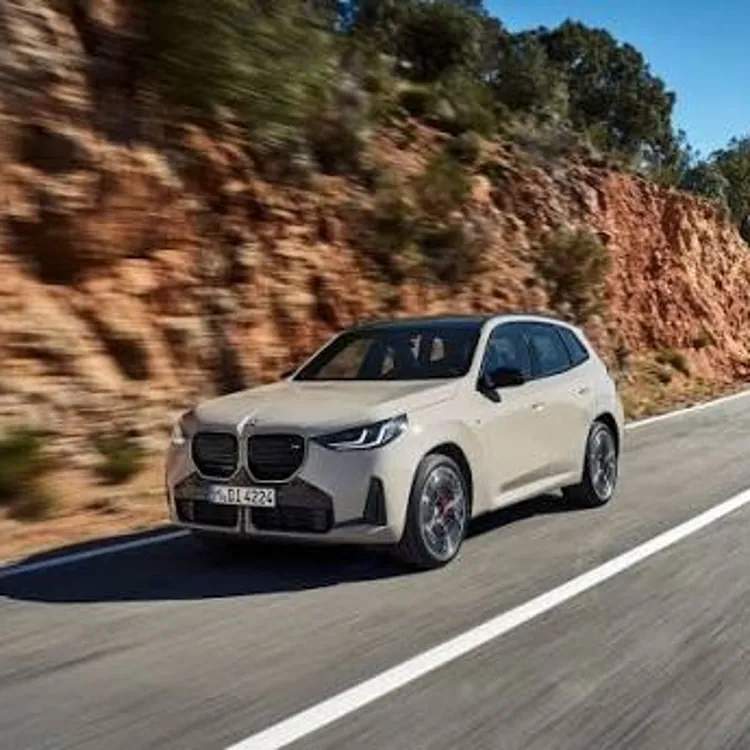 Beige SUV driving on a paved road next to a rocky hillside with trees