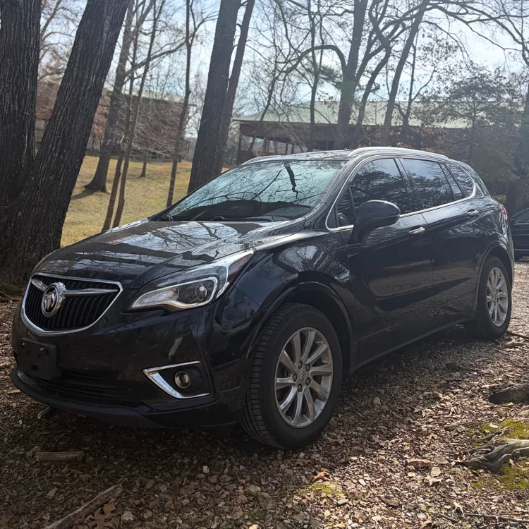 Black SUV parked on a forest path surrounded by tall leafless trees under a bright sky.