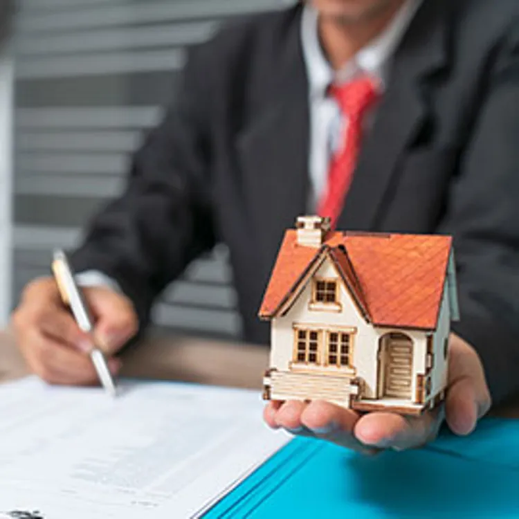 man writing with one hand while holding a miniature house with his other hand
