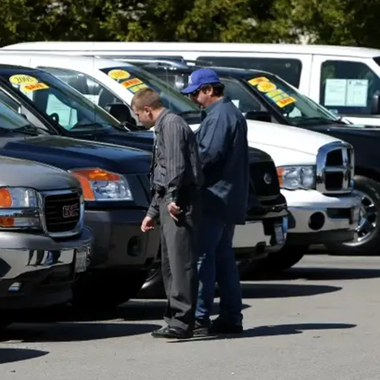 Two people inspecting pickup trucks parked in a row at a dealership lot