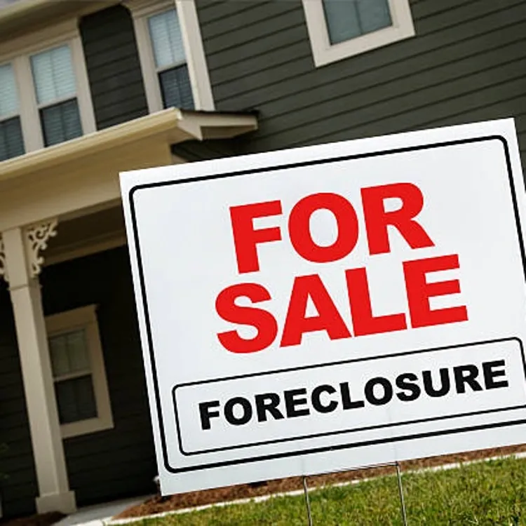 For sale foreclosure sign in front of a dark green suburban house