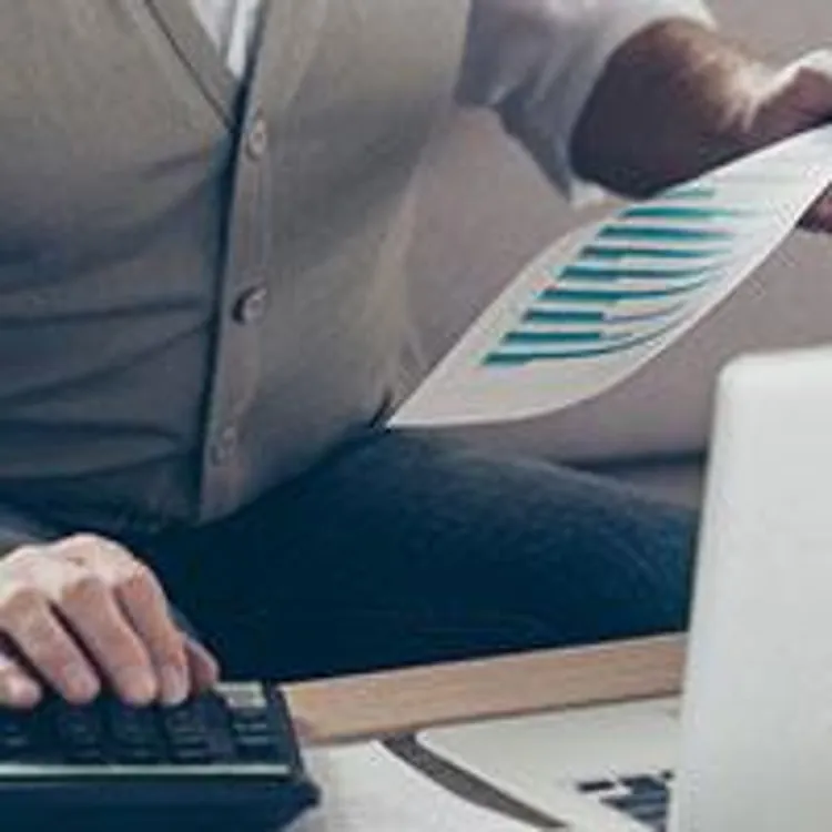 man using calculator and holding print out of a graph