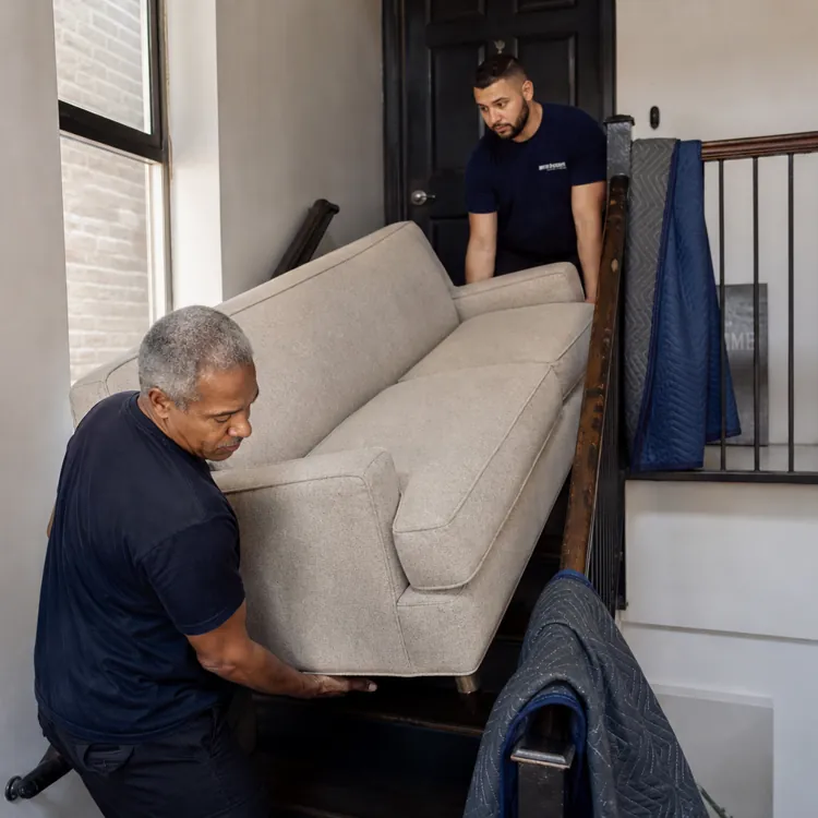 two men carrying a beige sofa up a staircase in a modern home
