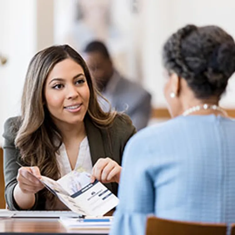 a cheerful female banker showing a customer an informational brochure