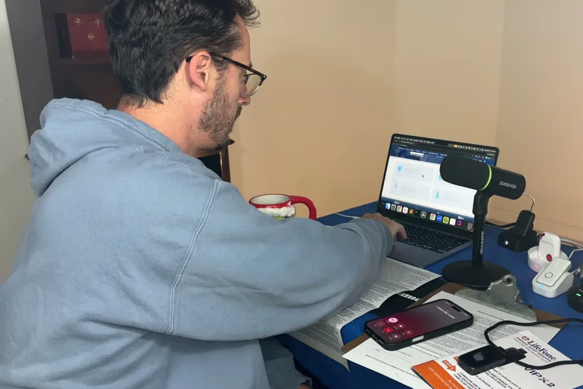 Chris Kolmar at his desk returning the LifeFone system, with several medical alert pendants, charging docks and the return paperwork on the table