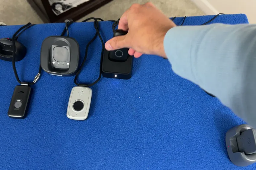 Chris Kolmar's arm reaching across a lineup of medical alert pendants and charging docks on a blue table