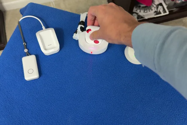 Chris Kolmar's hand on a medical alert charging dock in a row of pendants and docks on a blue table