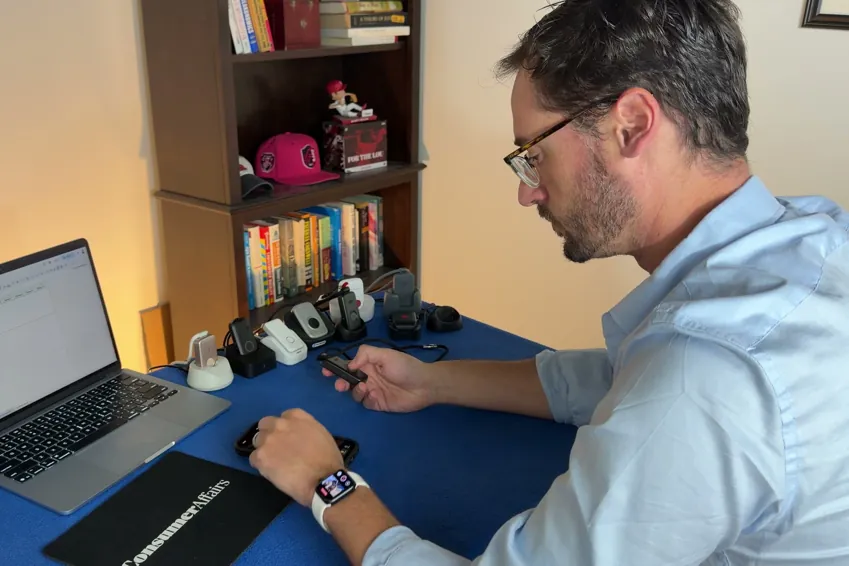 Chris Kolmar at a laptop testing medical alert devices, with several pendants and charging docks lined up on the table