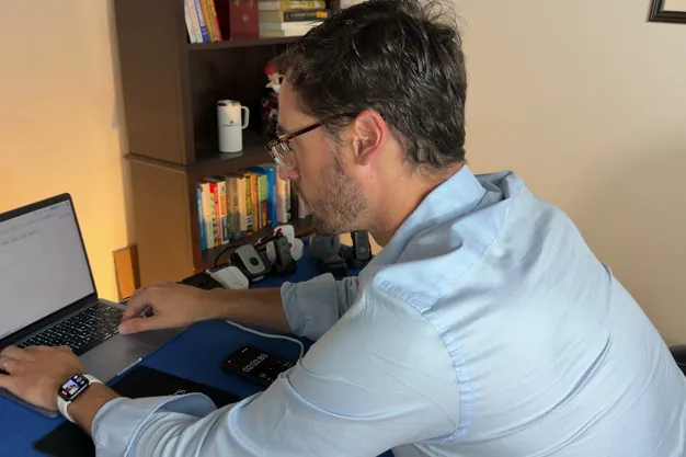 Chris Kolmar at a laptop testing medical alert devices, with several pendants and charging docks lined up on the table
