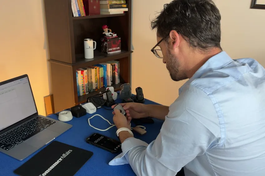 Chris Kolmar at a laptop testing medical alert devices, with several pendants and charging docks lined up on the table