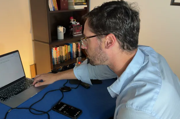 Chris Kolmar at a laptop testing medical alert devices, with several pendants and charging docks lined up on the table