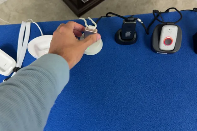 Chris Kolmar lifting a medical alert pendant out of its charging dock in a row of devices on a blue table