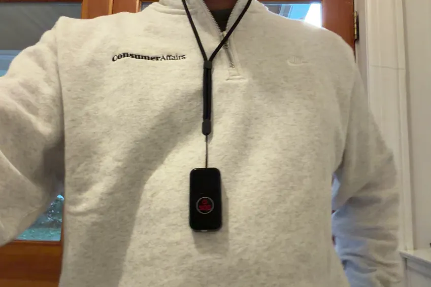 SecuLife SOS pendant hanging on its lanyard against a ConsumerAffairs quarter-zip