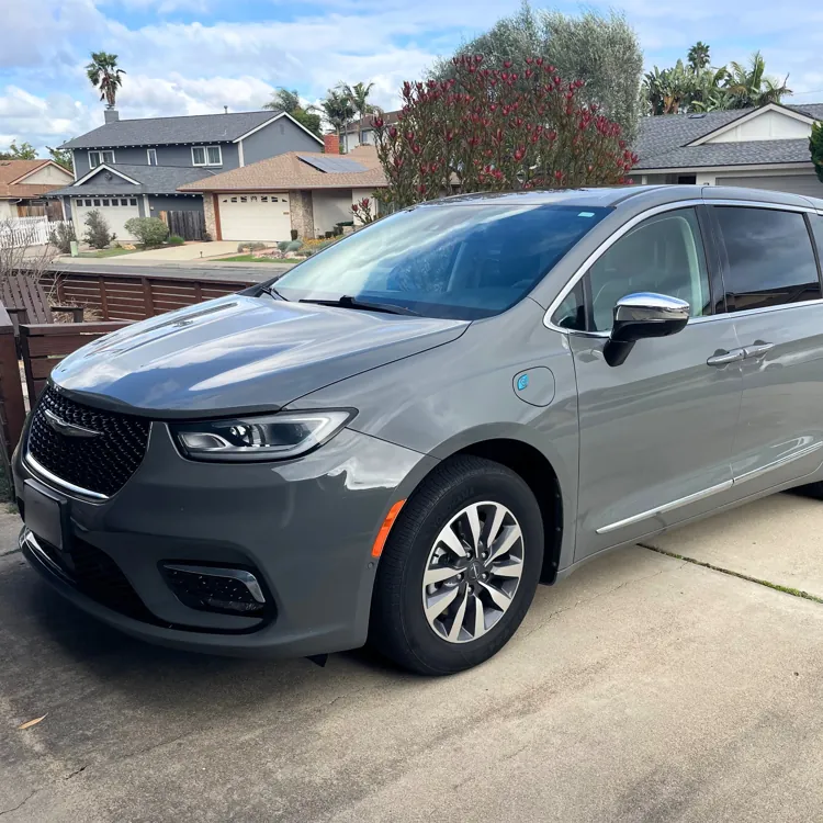 Gray minivan parked in a suburban driveway with houses and trees in the background.