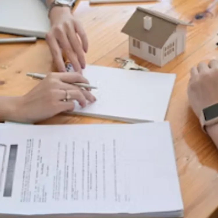 Two people reviewing documents with a small house model on a wooden table