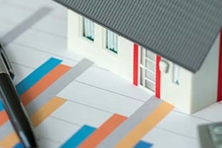 small model home and calculator sitting on bar charts