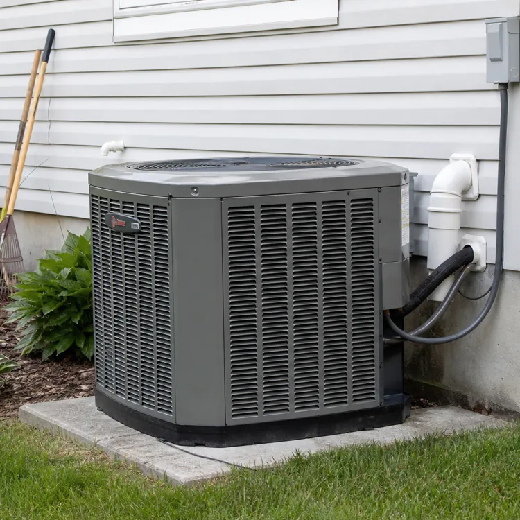 central air conditioning unit outside a house with garden tools and plants nearby