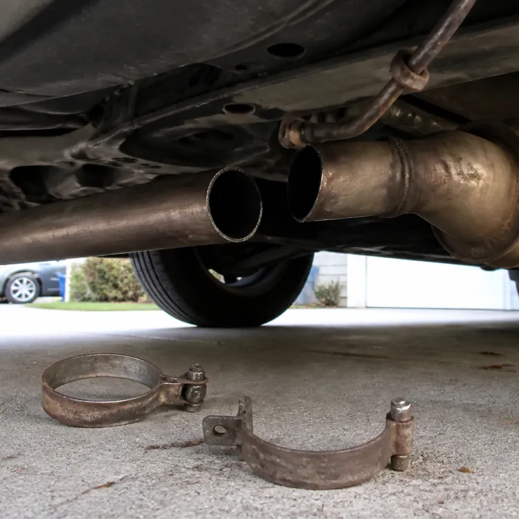 A car's undercarriage showing a detached catalytic converter and metal clamps on a driveway