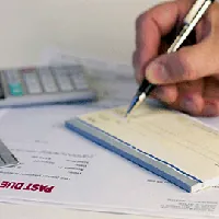 hand writing a check, bills and calculator on table