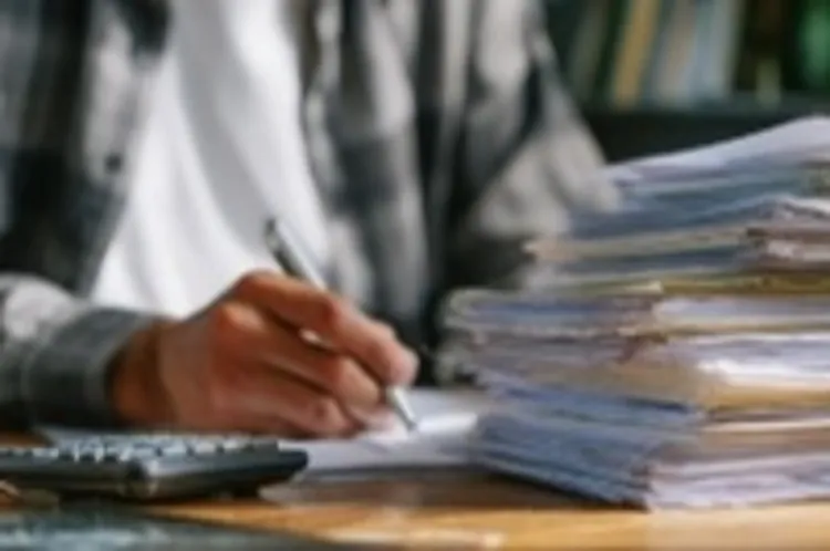 a man writing on a desk with a stack of papers on it