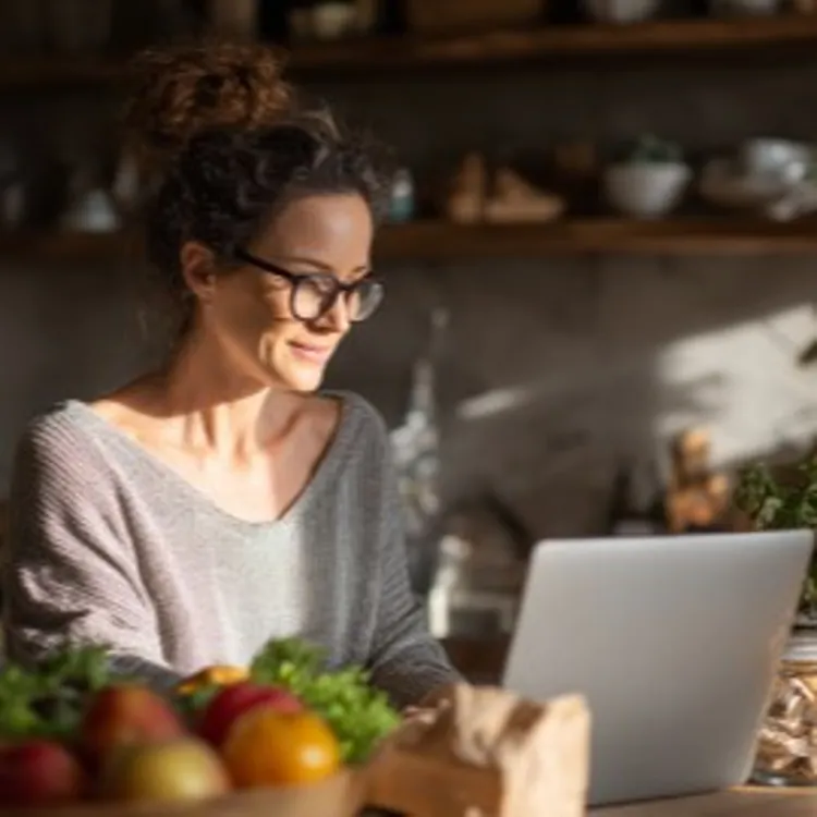 a woman sitting in her kitchen while browsing in her laptop