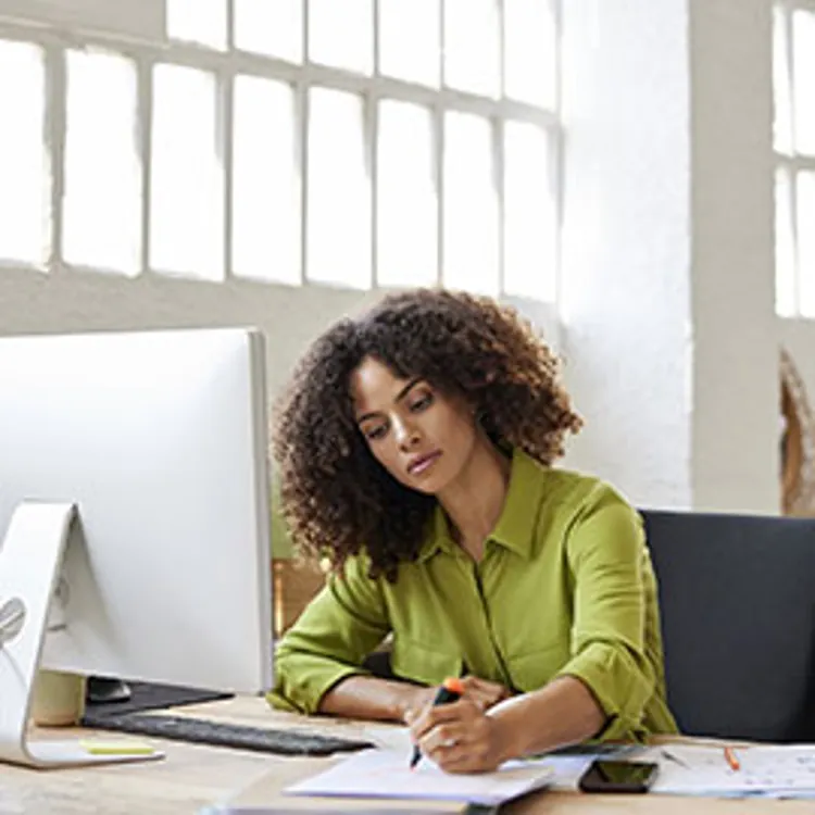 woman highlighting something on a document while sitting in front of a desk computer