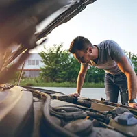 a young man looking under the hood of a car